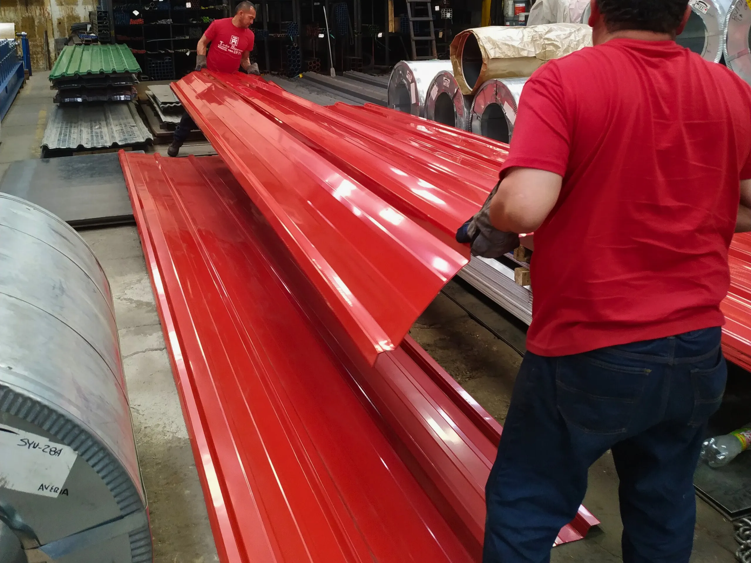 Equipo de Todo Hierros manejando láminas para techo de color rojo recién fabricadas en la planta.